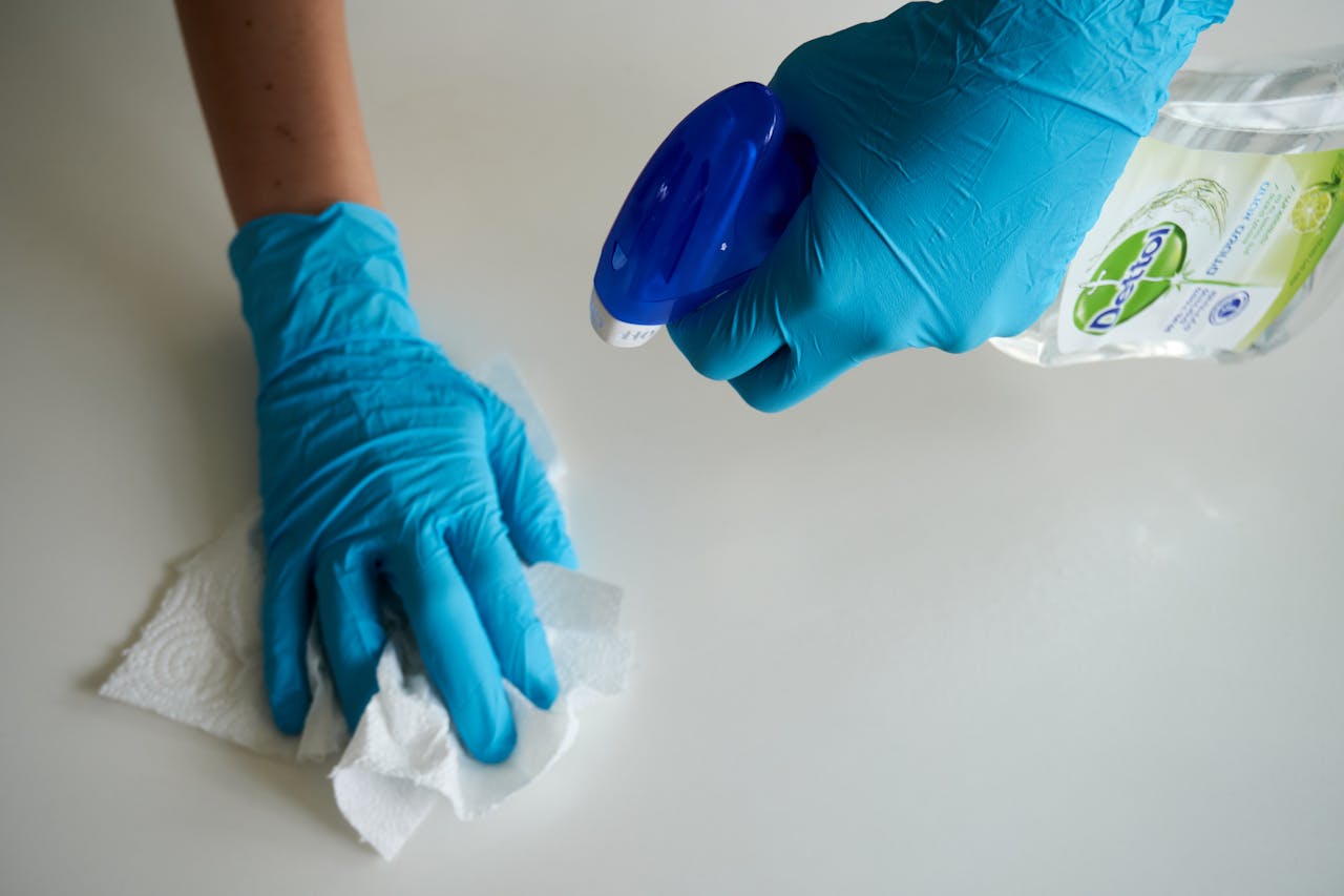 hero-img Close-up of hands wearing gloves cleaning a surface with disinfectant spray.