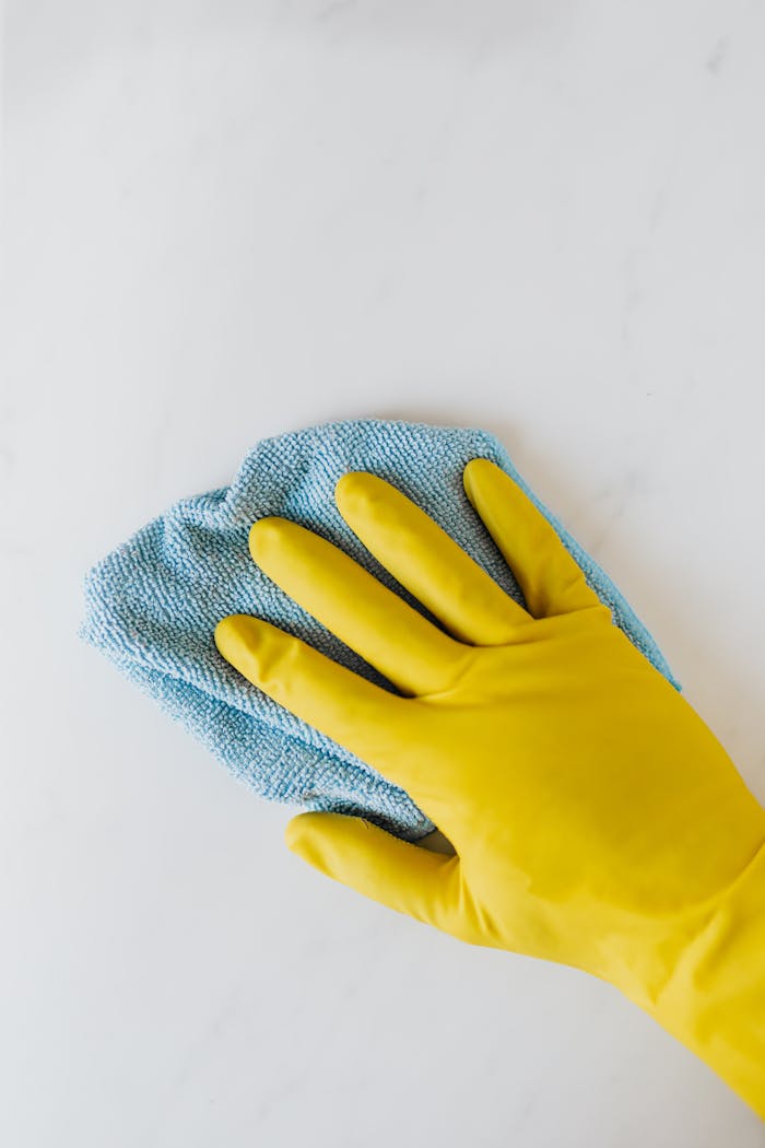 services-01 Yellow gloved hand wiping surface with blue cloth, concept of cleaning and hygiene.